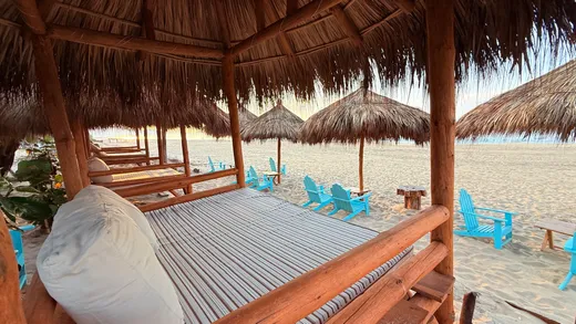 Camas balinesas bajo palapa y sillas azules en la playa