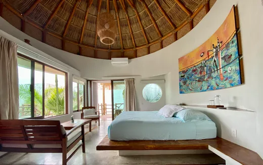 Habitacion redonda con techo de palapa, cama king y mural
